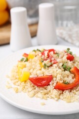 Plate of cooked bulgur with vegetables on white tiled table, closeup