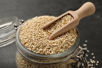 Dry quinoa seeds and scoop in glass jar on black table, closeup