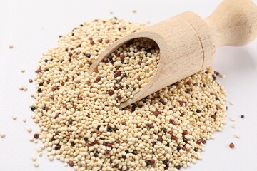 Scoop with raw quinoa seeds on white table, closeup