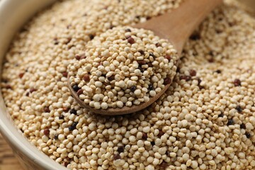 Raw quinoa seeds and spoon in bowl on table, closeup