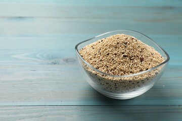 Raw quinoa seeds in bowl on light blue wooden table, closeup. Space for text
