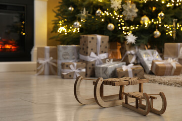 Wooden decorative sleighs in front of many gift boxes and Christmas tree on floor, selective focus. Space for text