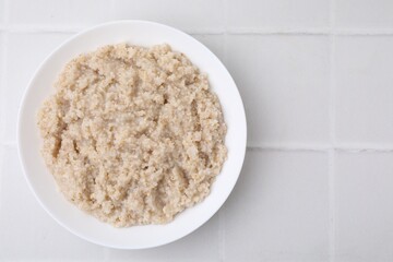 Delicious barley porridge in bowl on white tiled table, top view. Space for text