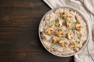 Delicious barley porridge with mushrooms and microgreens in bowl on wooden table, top view. Space for text