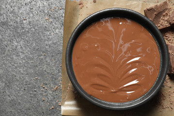 Melted milk chocolate in bowl on gray table, top view. Space for text