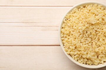 Delicious bulgur in bowl on wooden table, top view. Space for text