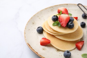 Delicious pancakes with berries and mint on white marble table, closeup. Space for text