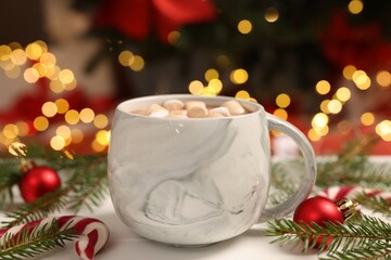 Delicious cocoa with marshmallows, Christmas decor and candy cane on table against blurred lights, closeup