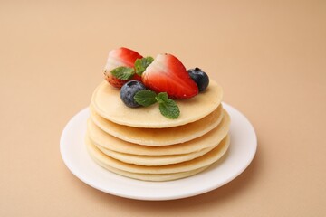 Stack of tasty pancakes with fresh berries and mint on beige background