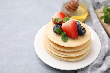 Stack of tasty pancakes with fresh berries, mint and honey on light grey table. Space for text