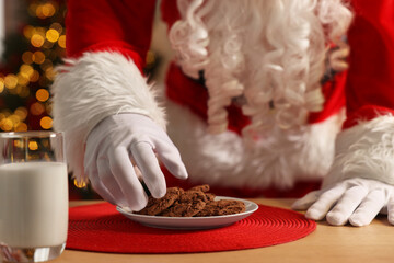 Merry Christmas. Santa Claus taking cookies from plate on table in room, closeup