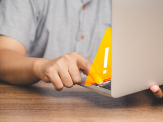 Young man using a laptop with a triangle caution warning sign for a notification error