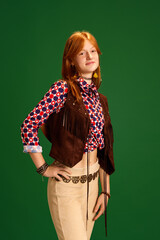 Half-length portrait of calm beautiful female fashion model with red hair dressed old-fashioned western style outfit posing against green studio background.