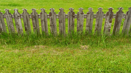 Old wooden picket fence in green grass as property boundary