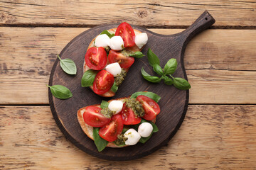 Delicious Caprese sandwiches with mozzarella, tomatoes, basil and pesto sauce on wooden table, top view