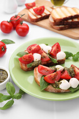 Delicious Caprese sandwiches with mozzarella, tomatoes, basil and pesto sauce on white tiled table