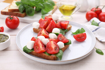 Delicious Caprese sandwiches with mozzarella, tomatoes, basil and pesto sauce on white wooden table