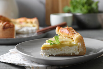 Piece of freshly baked rhubarb pie with cream cheese and mint leaves on grey wooden table, closeup