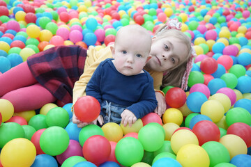 Fototapeta na wymiar A young girl and a little boy among bright multi-colored balls. Older sister and younger brother in the children's room.