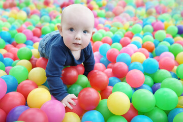 Fototapeta na wymiar A cute eared baby crawls among bright multi-colored balls. Cute baby in the children's room. Close-up portrait