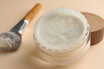 Rice loose face powder and makeup brush on beige background, closeup