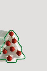 Plate as New Year tree wih shining red Christmas balls on white, Christmas tree from green glowing glass with star glare. Sunlight and shadow, sparkling holiday food, xmas still life