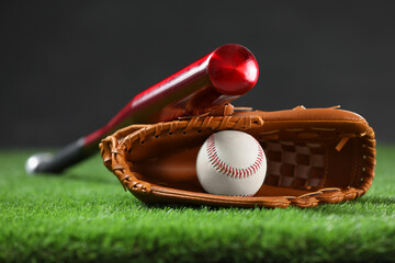 Baseball bat, leather glove and ball on green grass against dark background, closeup