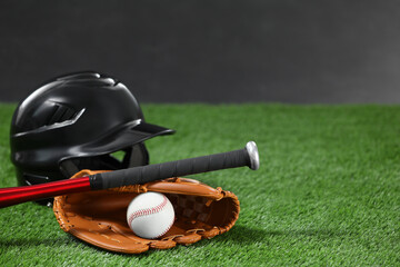 Baseball bat, batting helmet, leather glove and ball on green grass against dark background. Space for text