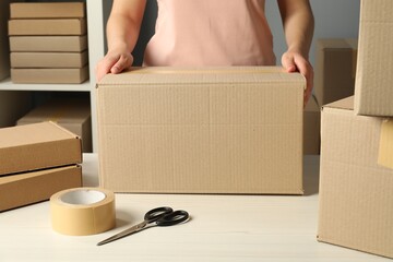 Packaging goods. Woman with cardboard boxes at white table indoors, closeup