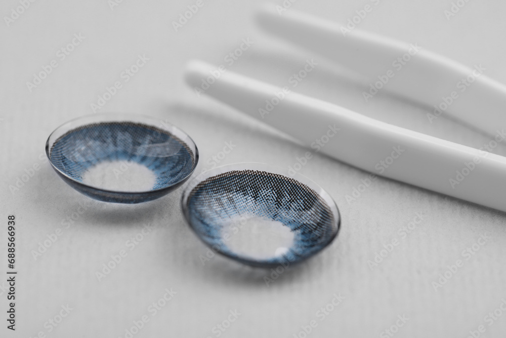 Poster Blue contact lenses and tweezers on white background, closeup