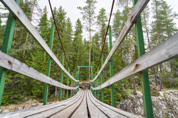 Wooden suspension bridge with handrails leading into forest