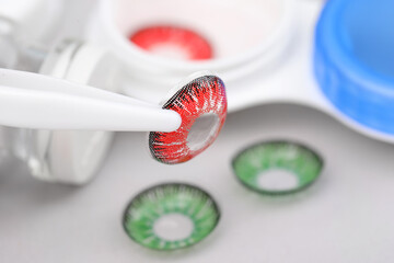 Tweezers with red contact lens on blurred background, closeup. Space for text