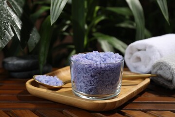 Bowl of purple sea salt, spoon and rolled towels on wooden table, closeup