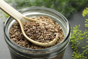 Jar with dry dill seeds and spoon on table, closeup