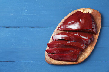 Cut raw beef liver on blue wooden table, top view. Space for text