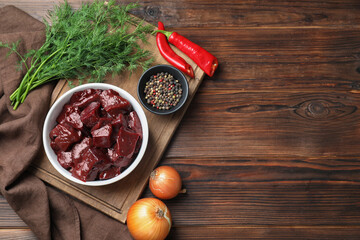 Cut raw beef liver with onions, spices, chili peppers and dill on wooden table, flat lay. Space for...