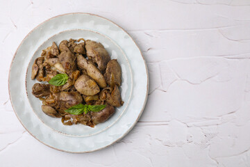 Plate of delicious fried chicken liver with onion and basil on white textured table, top view. Space for text