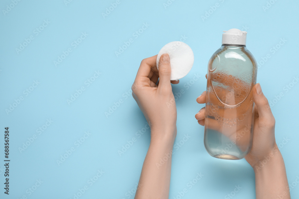 Wall mural woman holding makeup remover and cotton pad on light blue background, top view. space for text