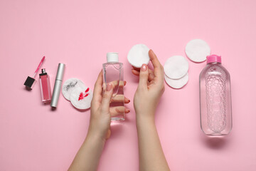Woman with makeup remover, cotton pads, cosmetic product, lip gloss and mascara on pink background,...