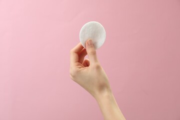 Woman holding cotton pad on pink background, closeup