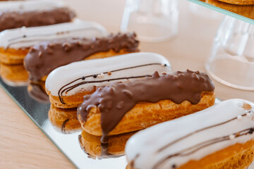 Eclairs with white and chocolate icing are laid out in a row on a mirror surface, display in a store.