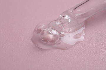Pipette with cosmetic serum on pink background, closeup