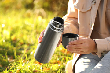 Woman with thermos and cup lid on green grass outdoors, closeup. Space for text
