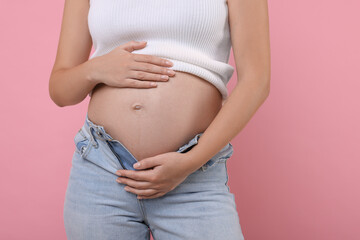 Pregnant woman in jeans on pink background, closeup
