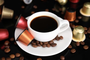 Cup of coffee, capsules and beans on black table, closeup
