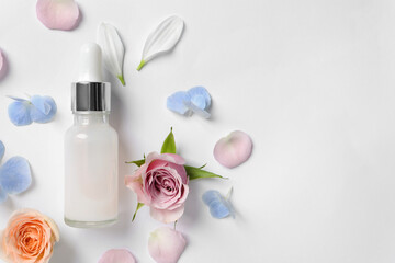 Bottle of cosmetic serum, beautiful roses and flower petals on white background, flat lay. Space...