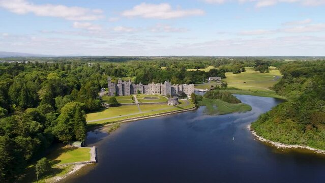 An orbital drone shot of Ashford Castle in Ireland. The camera moves and rotates from left to right around the front face of the castle.