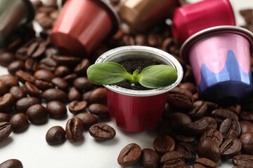 Coffee capsules with seedling and beans on white marble table, closeup