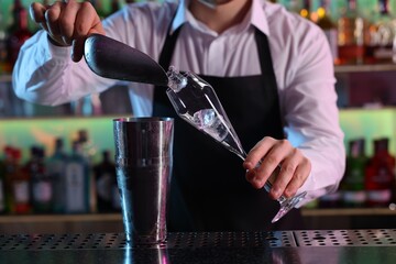 Alcoholic cocktail making. Bartender adding ice cubes into glass at counter in bar, closeup