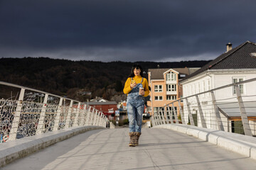 young adult woman walking through a city in Norway while looking at her cell phone